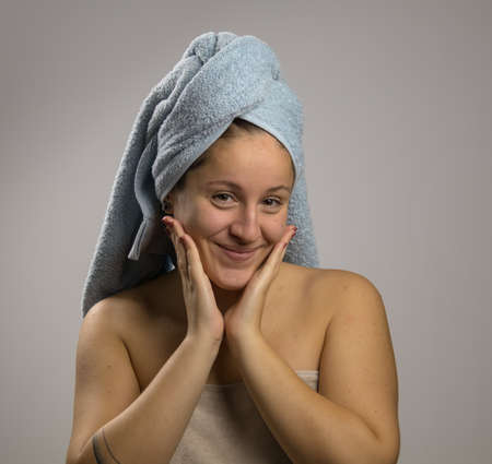 Girl after shower with a towel and smiling. Touching his faceの写真素材