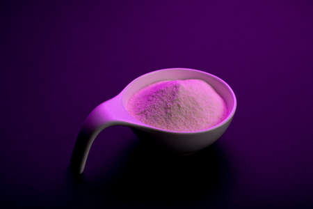 Whey protein powder sports bodybuilding supplement. Top view white porcelain scoop with vanilla flavor powder. Black background and purple lightの写真素材