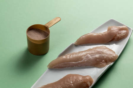 Raw chicken breasts and a whey protein scoop chocolate flavor. Sport nutrition. Green backgroundの写真素材