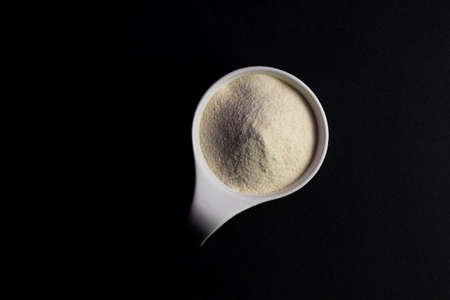 Whey protein powder sports bodybuilding supplement. Top view white porcelain scoop with vanilla flavor powder. Black backgroundの写真素材