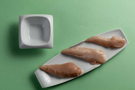 Raw chicken breasts and a clean mini plate on a green background. Elegant white plates. Top viewの写真素材