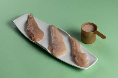 Raw chicken breasts and a whey protein scoop chocolate flavor. Sport nutrition. Green tableの写真素材