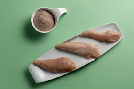 Raw chicken breasts and a whey protein scoop chocolate flavor. Sport nutrition. Green background. Top viewの写真素材