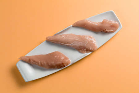 Raw chicken Breasts on a orange table. Elegant white plate. top viewの写真素材