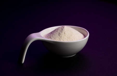 Whey protein powder sports bodybuilding supplement. Top view white porcelain scoop with vanilla flavor powder. Black background and purple lightの写真素材
