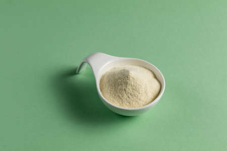 Whey protein powder sports bodybuilding supplement. White porcelain scoop with vanilla flavor powder. Solid color: greenの写真素材