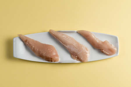 Raw chicken Breasts on a yellow background. Elegant white plate. Top viewの写真素材