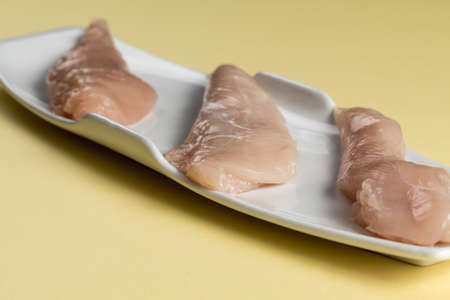 Raw chicken Breasts on a yellow table. Modern white plateの写真素材