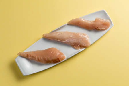 Raw chicken Breasts on a yellow background. Elegant white plate. top viewの写真素材