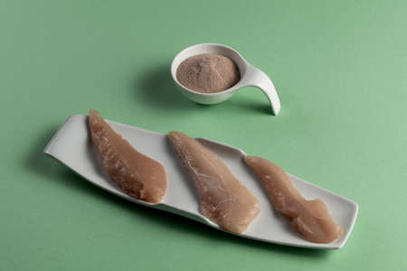 Raw chicken breasts and a whey protein scoop chocolate flavor. Sport nutrition. Green tableの写真素材