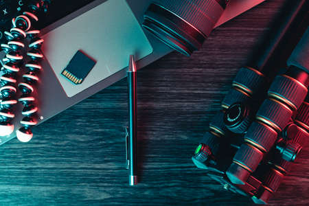 Top view of a desk working with laptop keyboard, modern camera, tripod and a black pen on a wood background. Freelance, creative or online education concept. Red and blue lightの写真素材