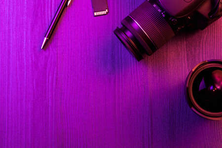 Camera, pen, fish eye lens and SD card. Pink light. Workspace top view. Copy space. Wood backgroundの写真素材