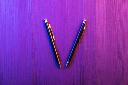 Two elegant pen on wood background and pink and blue light. Business black pen. Top viewの写真素材