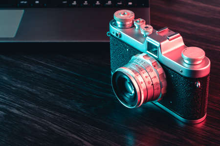 Old film camera and laptop on table. Blue and red light.の写真素材
