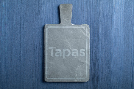 Black slate board for serving with copy space, top view, on wood table background. Spanish Tapas