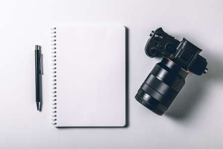 Modern white office desk table with pen and digital camera mirrorless. Blank notebook page for input the text in the middle. Top view, flat lay.の写真素材