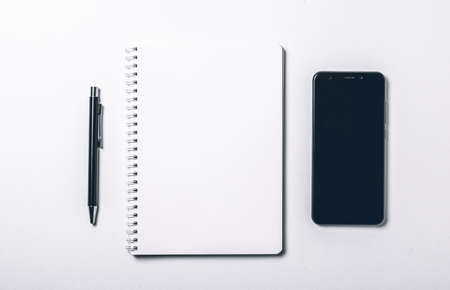 Modern white office desk table with pen and smart phone. Blank notebook page for input the text in the middle. Top view, flat lay.の写真素材