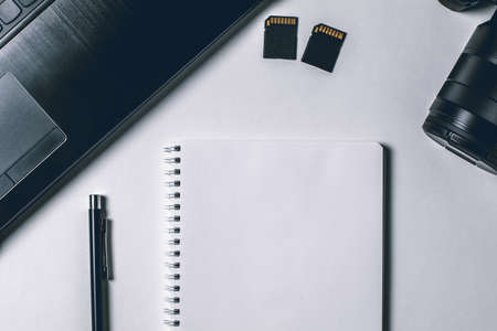 Modern white office desk table with laptop, camera and other supplies. Blank notebook page for input the text in the middle. Top view, flat lay.の写真素材