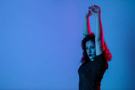 Emotional portrait, a girl with her hands up. Color light, blue and red. Studio shot. Copyspace for insert textの写真素材