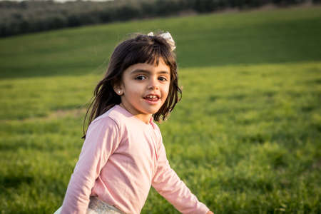 little girl smiling and walking with pink shirt in a meadowの写真素材