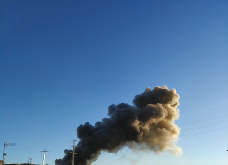 Huge plume of black smoke from fire rising high above flat land against blue sky. Seville, Spain
