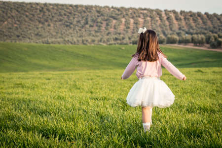 little girl walking with pink shirt and skirt in a meadowの写真素材
