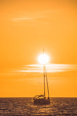Little white boat floating on the water towards the horizon in the rays of the setting sunの写真素材