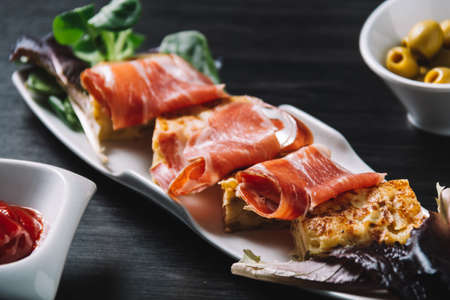delicious Spanish potato omelette top with serrano ham, and olivesの写真素材
