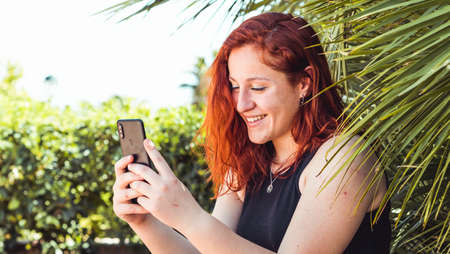 Happy girl watching media in a smart phone sitting in the parkの写真素材
