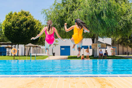 Two teenage girls jumping in a swimming pool. Two girls jumping into a swimming poolの写真素材