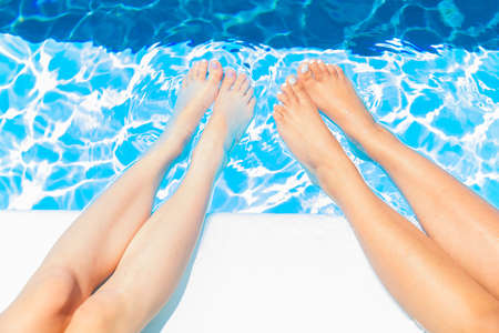 Young girls sit on the edge of swimming pool and chat with their feet in the waterの写真素材