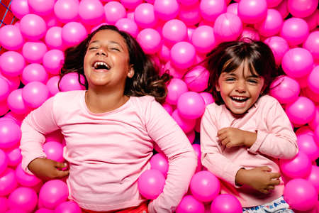 two little girls smiling and playing at pink ball poolの写真素材