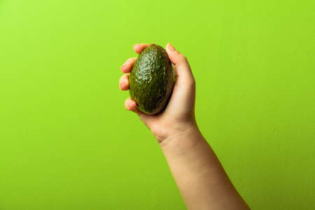 avocado in a hand of woman green background. healthy food conceptの写真素材