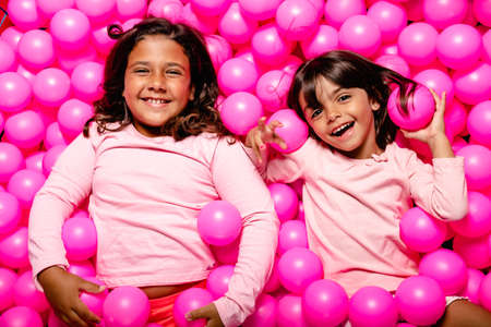 two little girls smiling and playing at pink ball poolの写真素材
