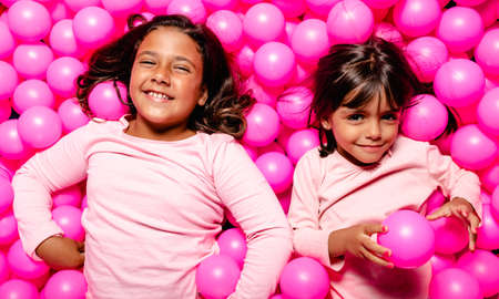 two little girls smiling and playing at pink ball poolの写真素材