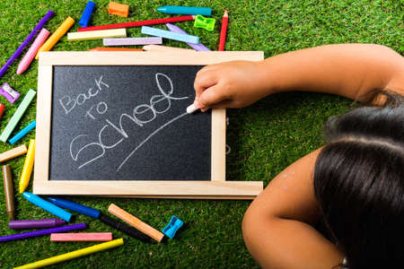 Back to school supplies arrangement vivid colorful on green grass and blackboard hand chalkの写真素材