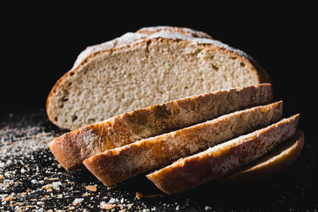 Sliced loaf of dark homemade bread dusted with flour on darkの写真素材