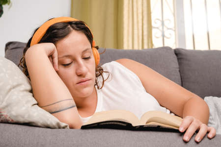 woman with headphones reading a book in the living room sitting on the couchの写真素材