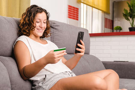 woman on the living room couch shopping online with a credit card and a smartphoneの写真素材