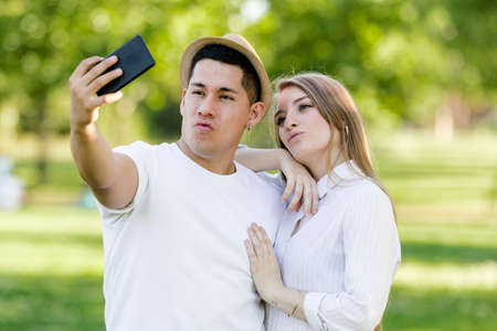 Young couple taking a selfie on their mobile in the park. Latin man and Caucasian womanの写真素材