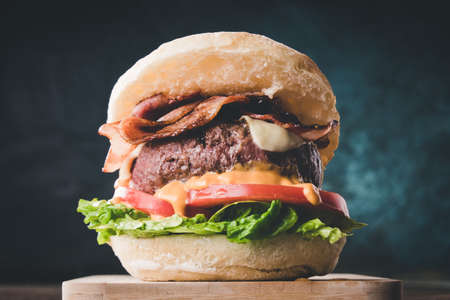 View of fresh tasty burger on wooden table. Hamburger with bacon, cheese, lettuce, tomato and sauceの写真素材