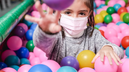 happy 5 year old girl with mask in a ball pool throwing balls to cameraの写真素材