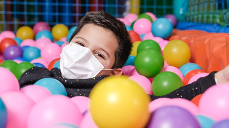 happy 5 year old boy with mask in a ball pool throwing balls to cameraの写真素材