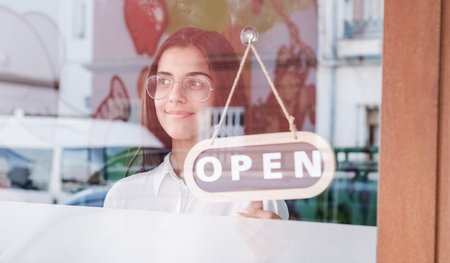 Happy small business girl changing closed to open sign on window smiling looking outsideの写真素材
