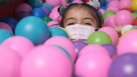 happy 5 year old girl with mask in a ball pool throwing balls to cameraの写真素材