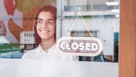 Happy small business girl changing closed to open sign on window smiling looking outsideの写真素材