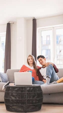 Young couple on a video call with their laptop while sitting on a couch together at home.の写真素材