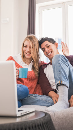 Young couple chatting with friends or family on a video call with their laptop while staying at home.の写真素材