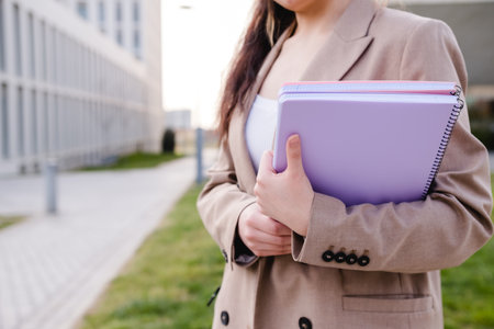 Unrecognizable student holding folders while standing outside college campus. Education concept.の写真素材