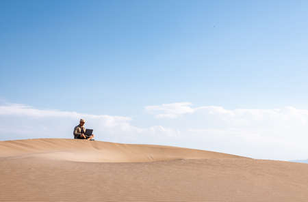 Man using laptop on sand duneの写真素材